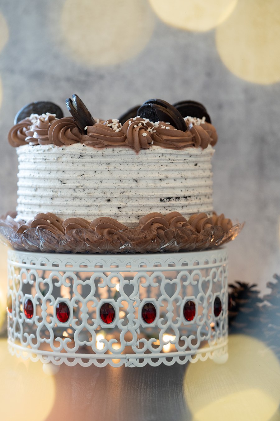 A cake with Oreo and chocolate frosting and Oreo cookies sits on a decorative cake stand.