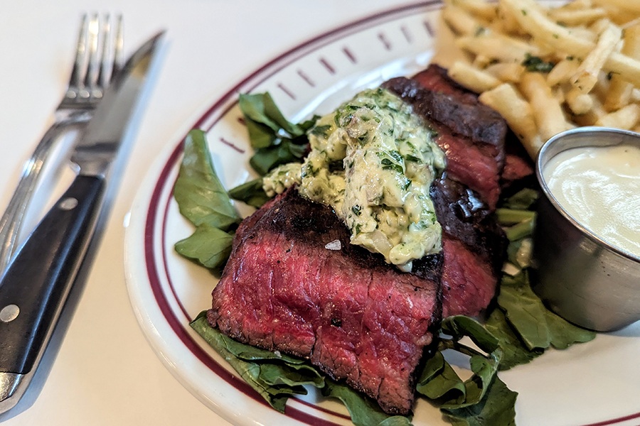 Sliced rare steak is topped with herb butter and served with fries.