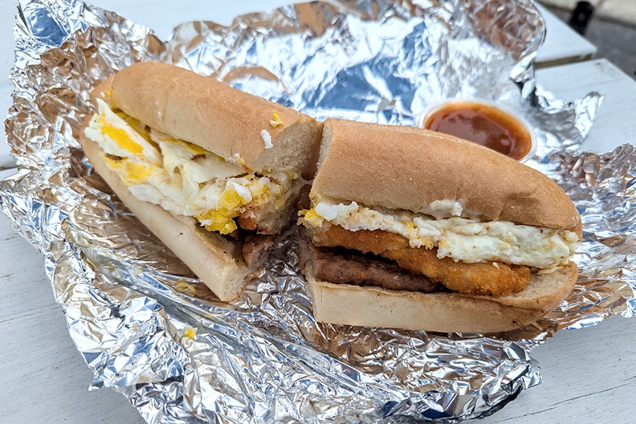 Breakfast sandwich on a sub roll, sliced in half, with sausage, egg, and hash brown.