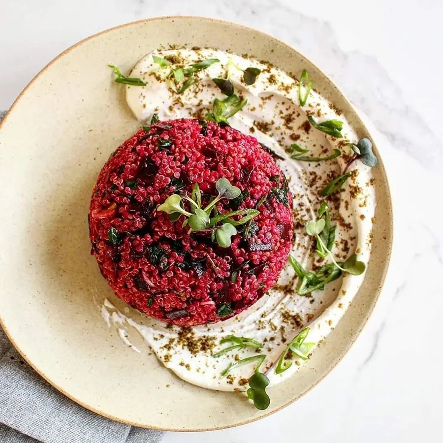 Overhead view of a scoop of purple quinoa with chunks of beets, sitting atop a swoosh of herby feta.