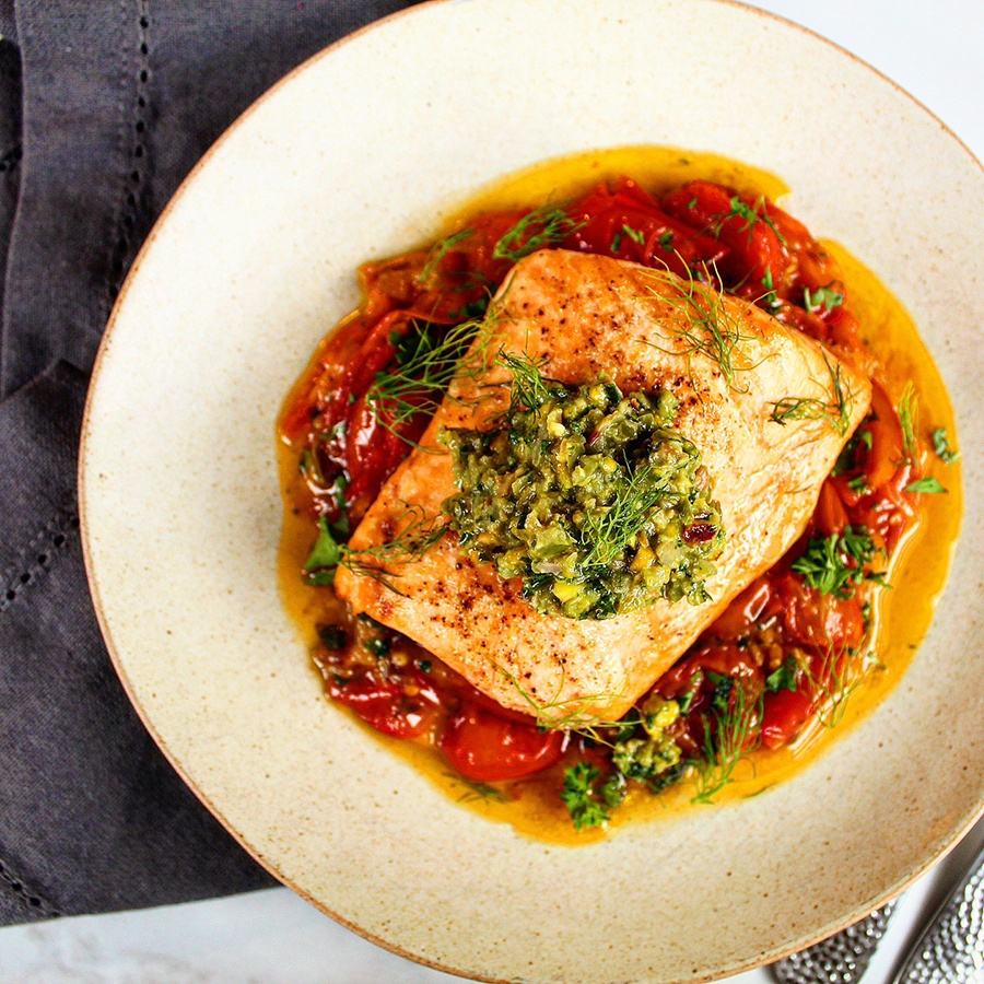 Overhead view of a piece of cooked salmon over roasted tomatoes and topped with a green salsa.