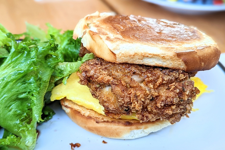 Fried chicken and egg sit on a thin bun next to some lettuce on a plate.