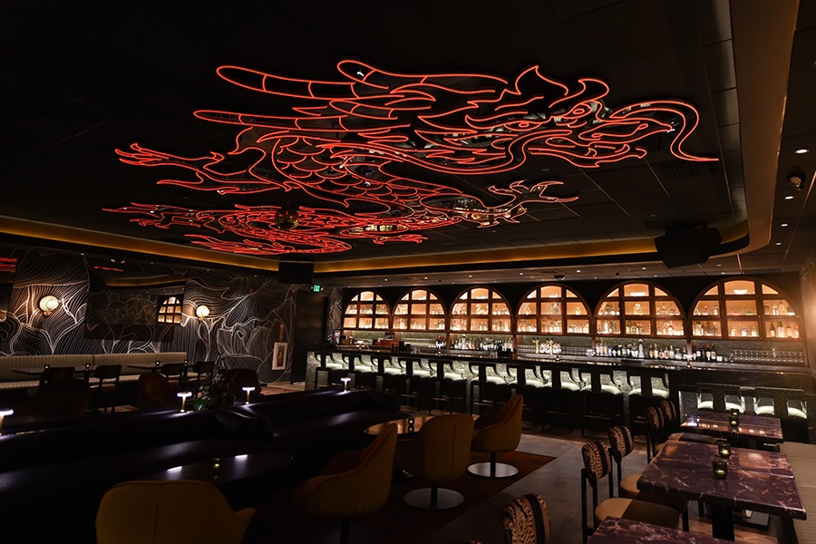 Dimly lit interior of a lounge-like restaurant with an illuminated red dragon decorating the ceiling.