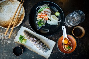 Overhead view of sashimi and other Japanese food on a dark table.