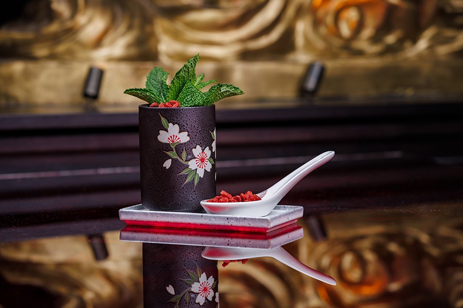 A cocktail is presented in a black mug with flowers on it, with a fresh mint garnish.