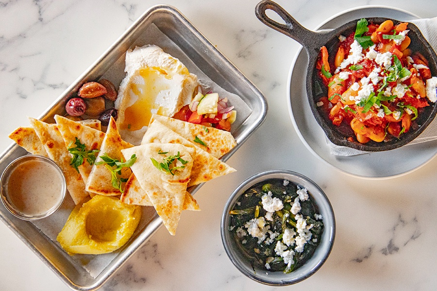 Overhead view of pita with dips and other Mediterranean food on a white marble table.