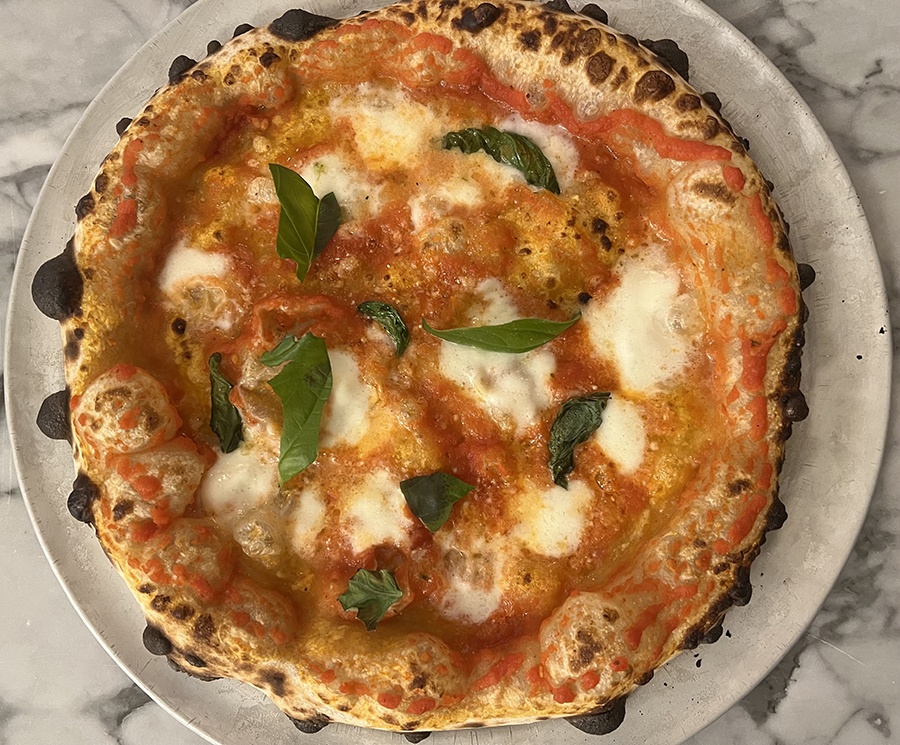 Overhead view of a Neapolitan-style Margherita pizza with fresh basil and an airy crust with spots of char.