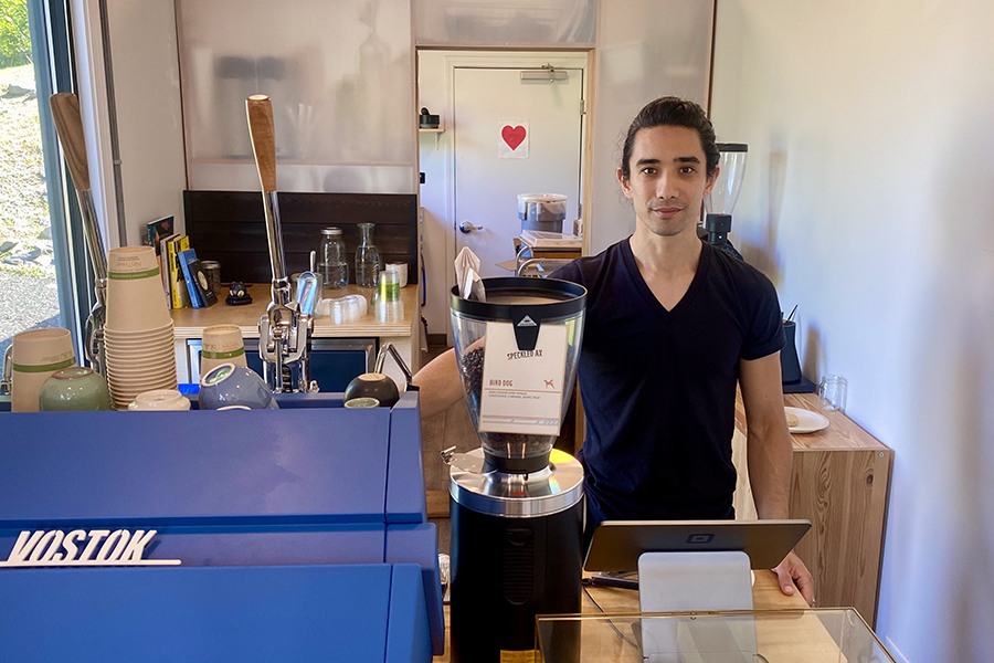 A man stands at the register of a small coffee shop.