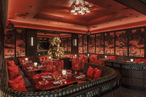 A lounge space in a restaurant is ornately decorated with Chinese-inspired murals, red satin chair coverings, and a gold dragon.