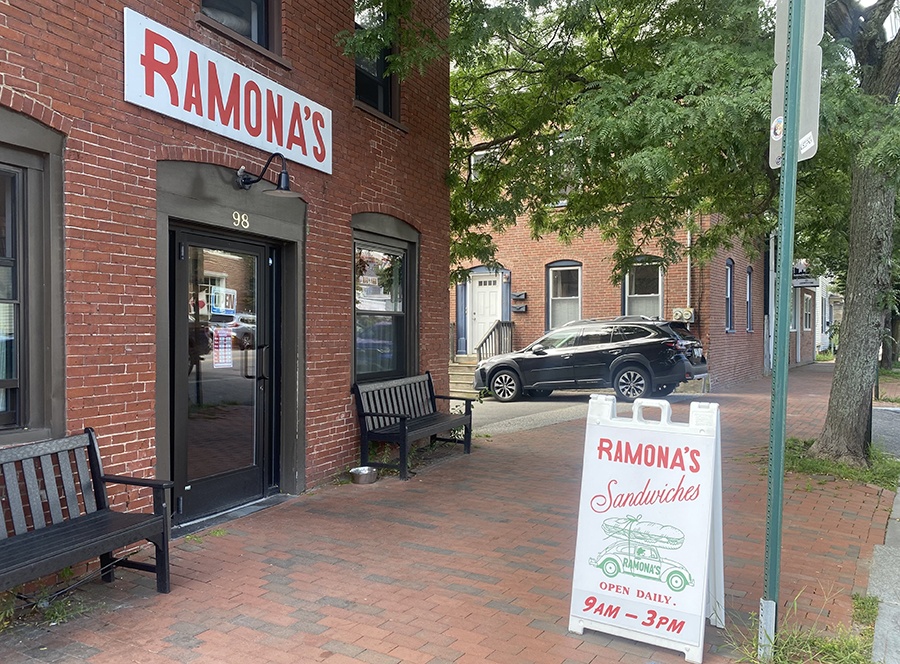 White signage on a red brick building says Ramona's in capital red letters. A sandwich board out front advertises sandwiches.