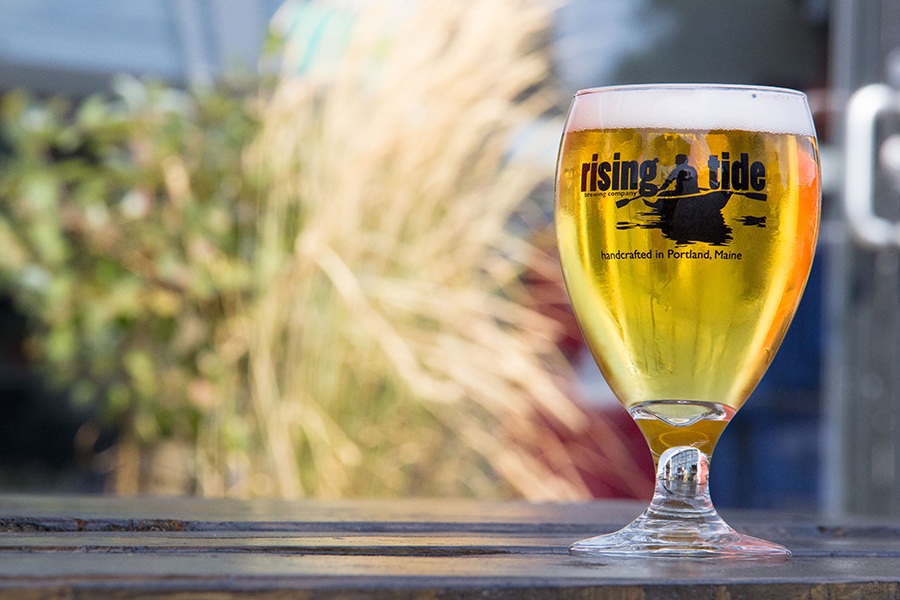 A glass of beer on a picnic table has Rising Tide branding with an image of a person canoeing.