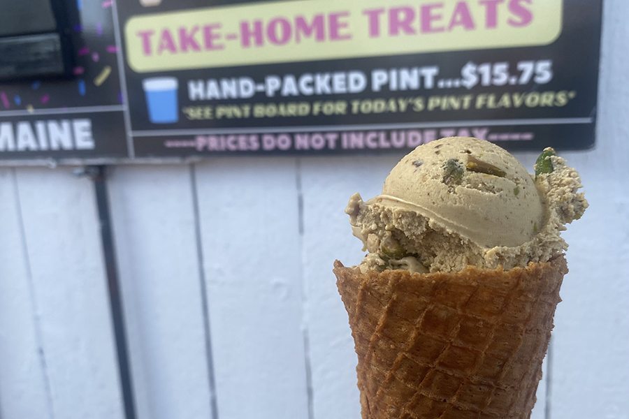 A cone of green pistachio ice cream in front of a sign with pricing for ice cream pints.