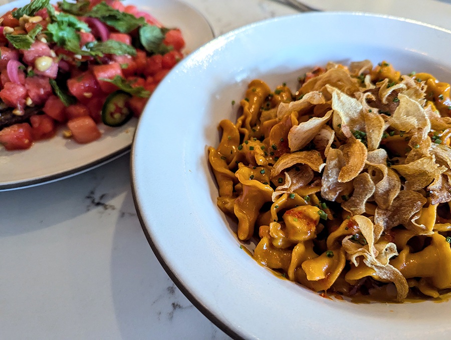 Twists of pasta are studded with chunks of lobster. A dish full of watermelon cubes sits in the background.