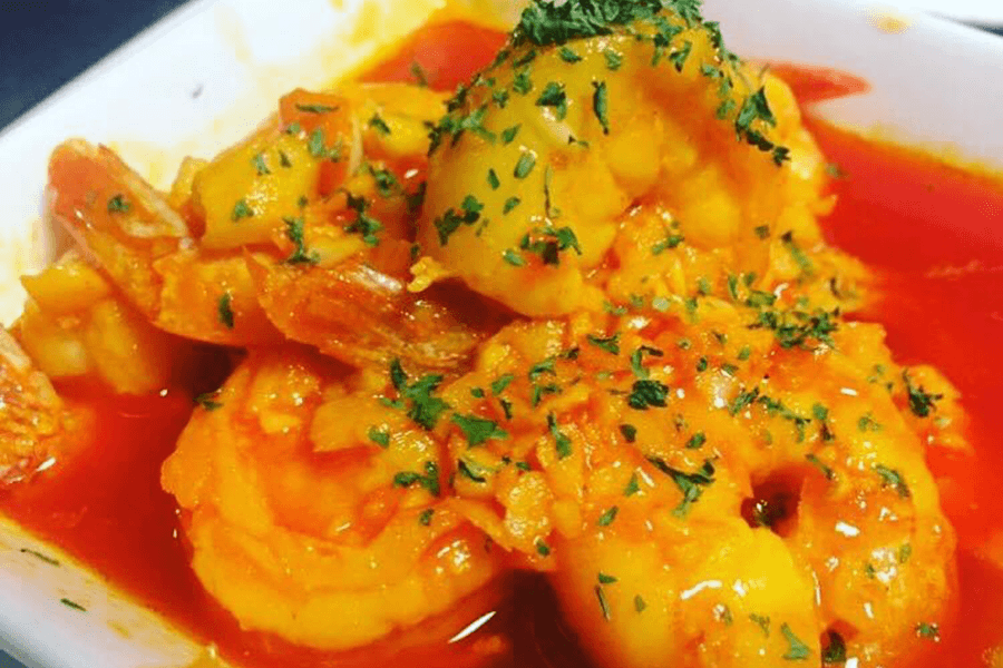 Plump shrimp sit in a bright red broth and are topped with finely chopped herbs.