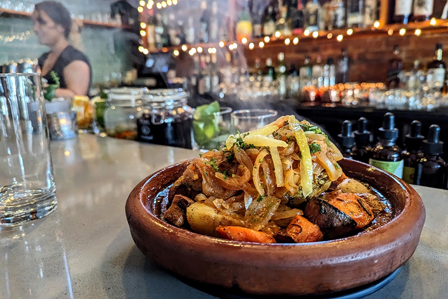 A chicken dish in a round brown bowl, with steam coming out, sits on a restaurant bar.