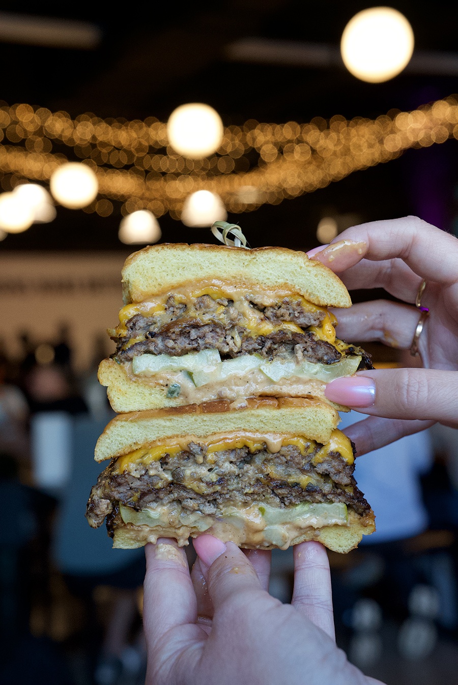 Hands hold a burger, cut in half, with cheese, onions, and special sauce.