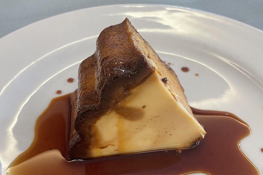 A custardy dessert sits on a plate in a thin pool of brown sauce.