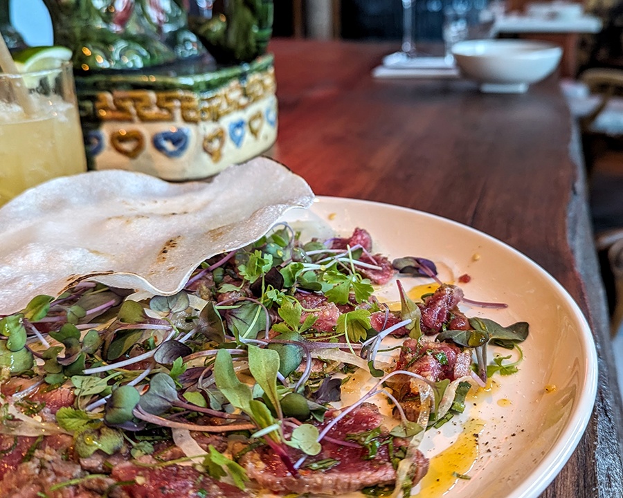 Rare slices of beef are topped with lots of fresh herbs, a rice cracker, and a drizzle of oil.