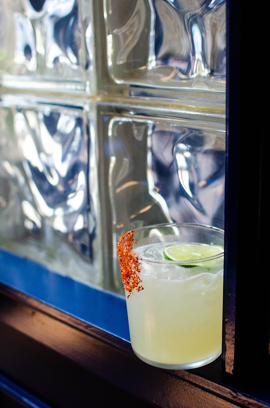 A margarita sits against a glass block window.