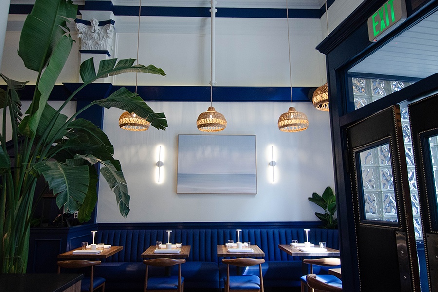 A restaurant interior features a royal blue banquette and accents, wicker lamps, and greenery.