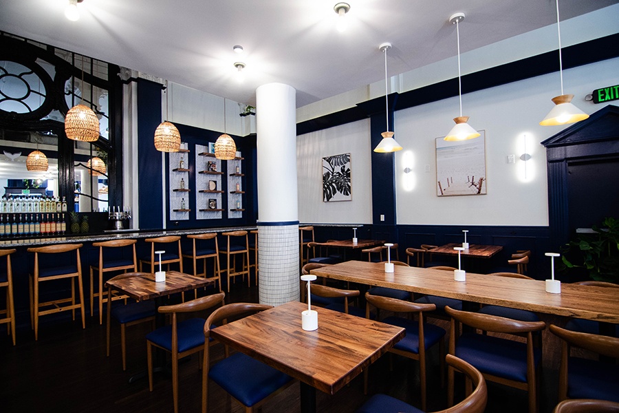 A restaurant interior features glossy wooden tables, royal blue accents, and a giant mirror behind a bar.