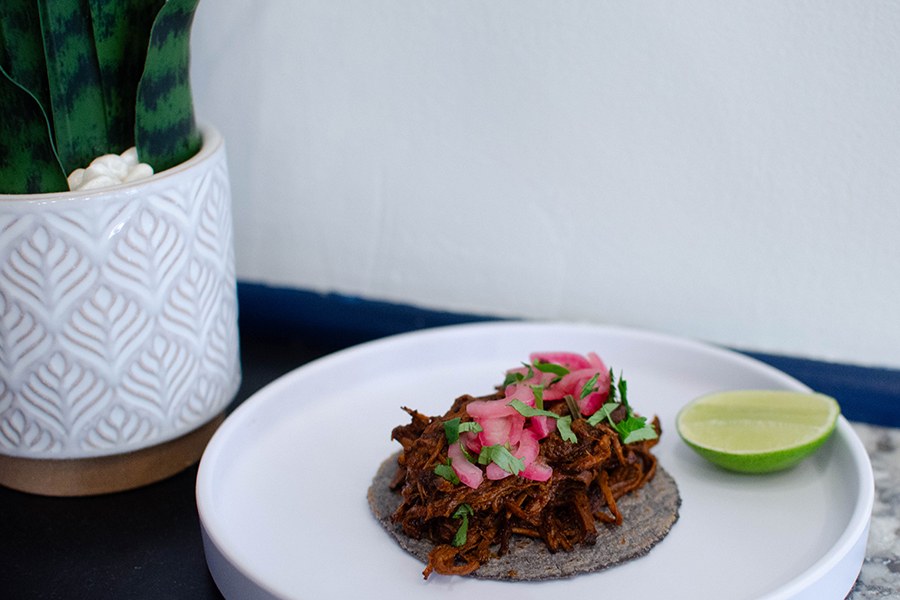 A blue corn tortilla is topped with shredded beef, red onions, and cilantro.