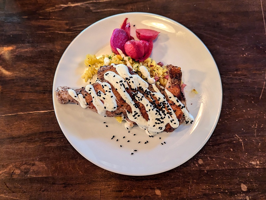 Chicken is drizzled with a thick white sauce and black sesame seeds, served atop yellow rice.