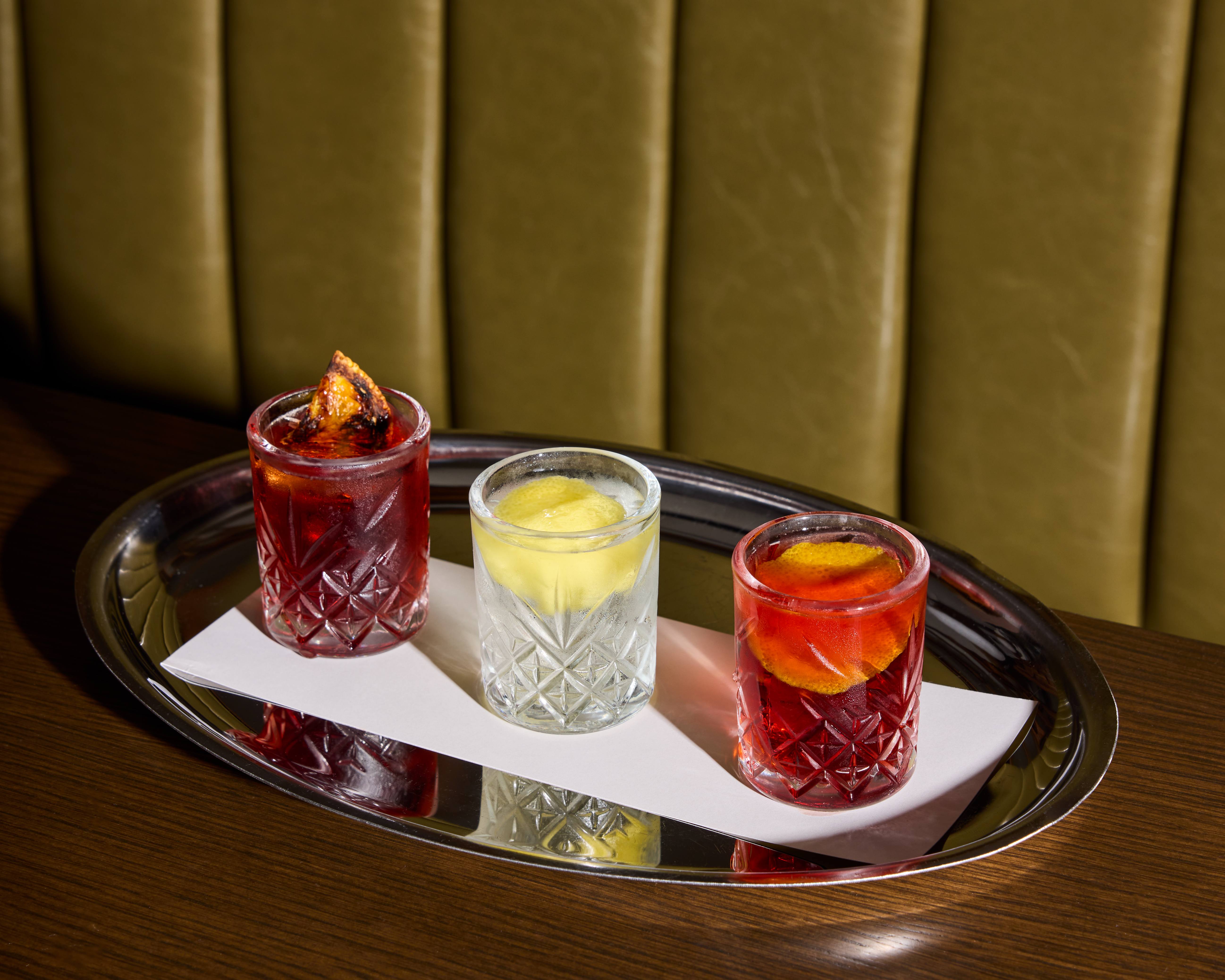 Three small etched glasses are full of alcohol and citrus garnishes.