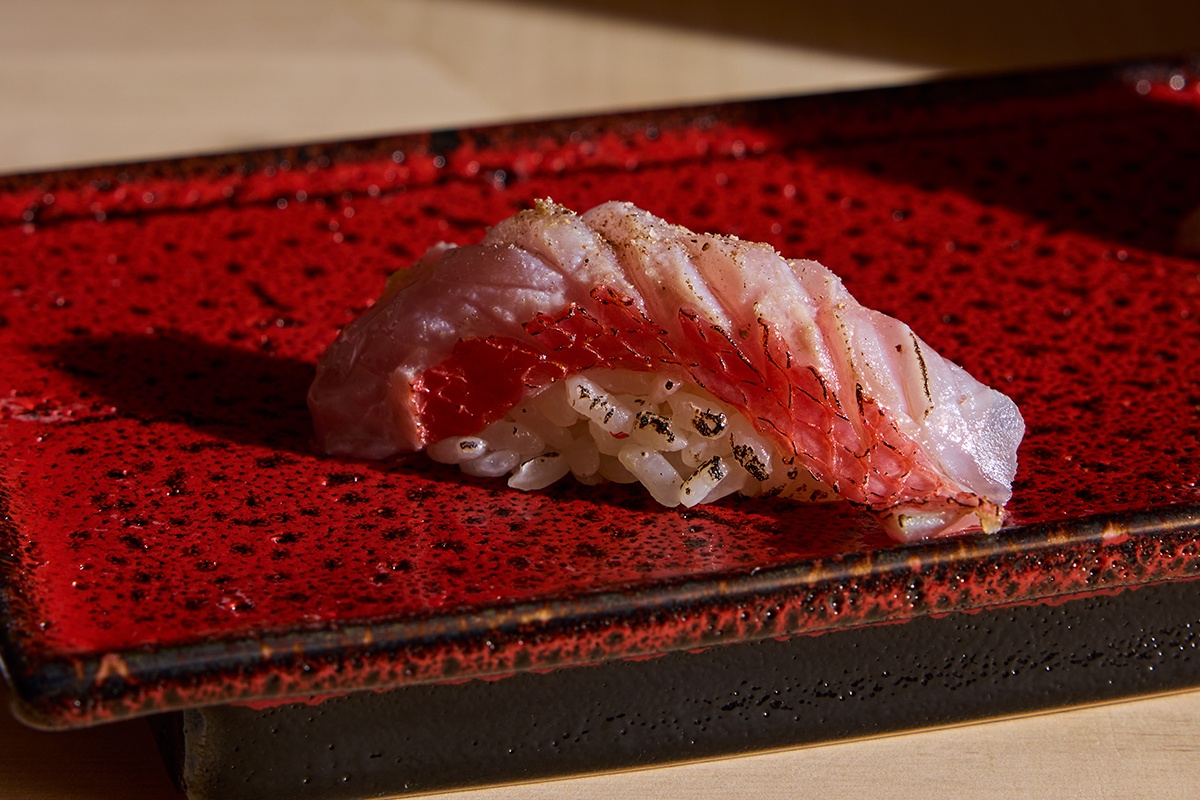 A piece of nigiri sushi on a rectangular maroon plate.