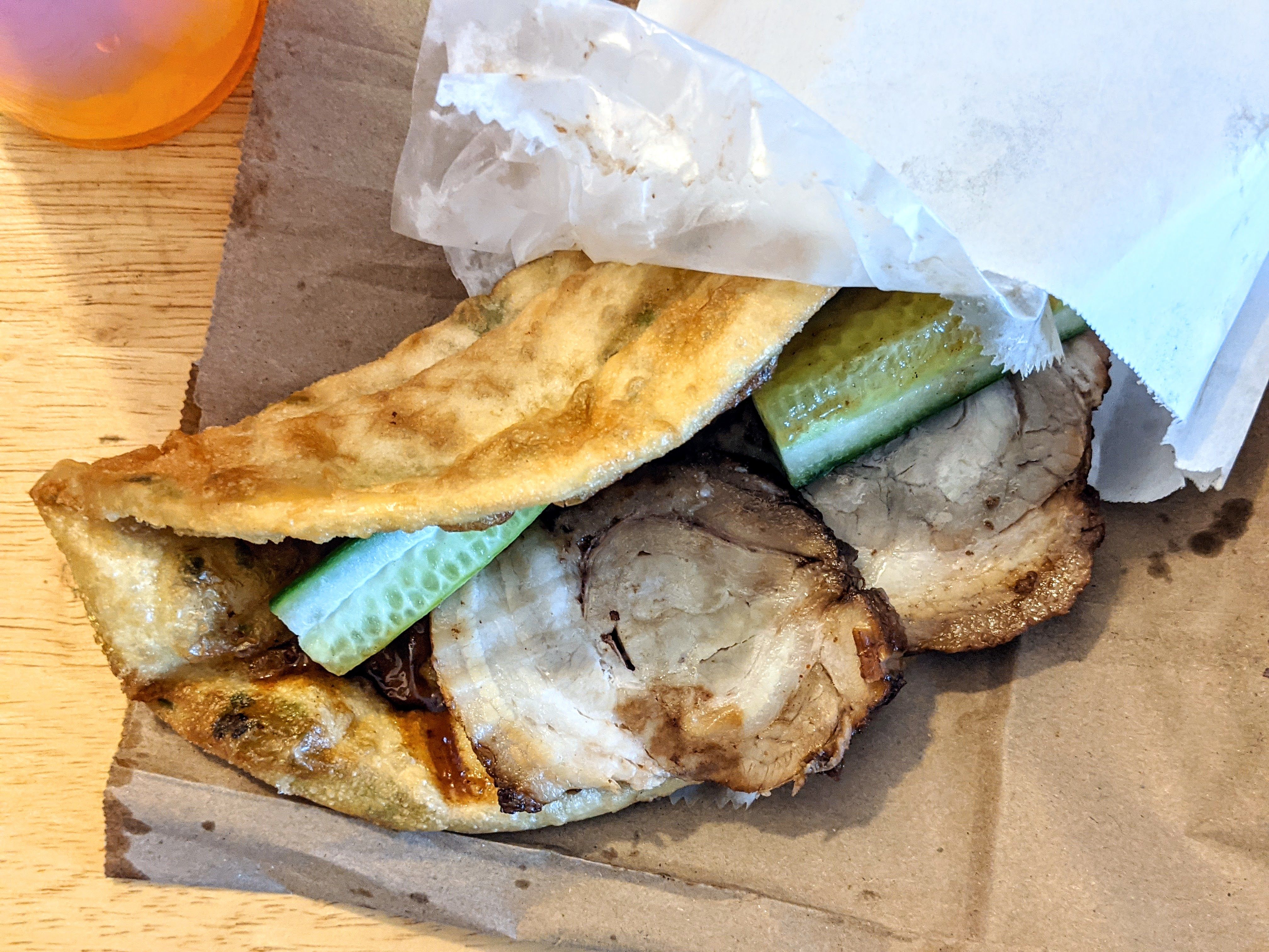 A scallion pancake is stuffed with slices of pork and cucumber.