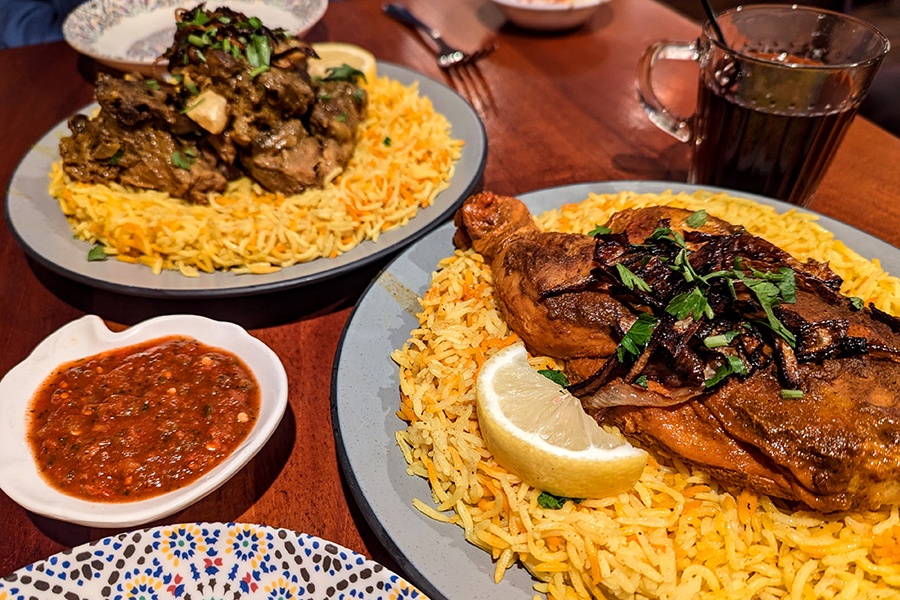 Lamb and chicken dishes over yellow rice with lemon wedges and caramelized onion.