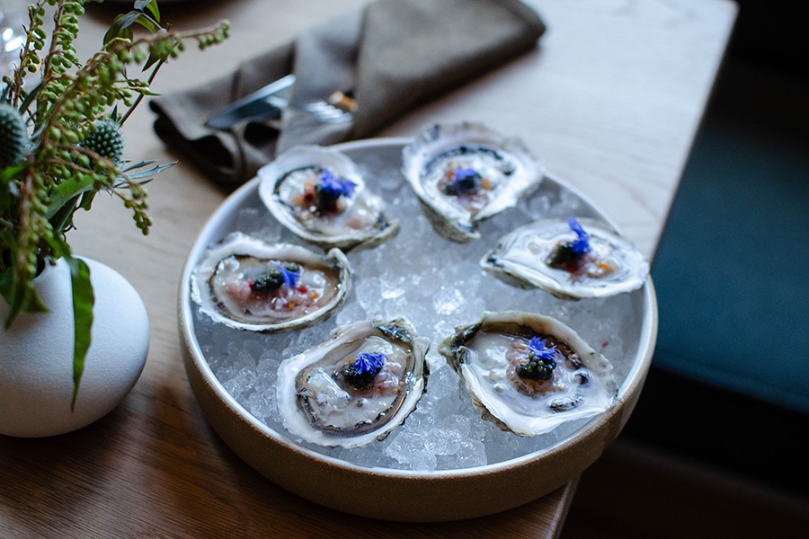 Half a dozen oysters on ice, garnished with caviar and a purple flower petal.