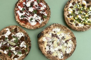 Overhead view of four different Neapolitan-style pizzas on a pale green background.