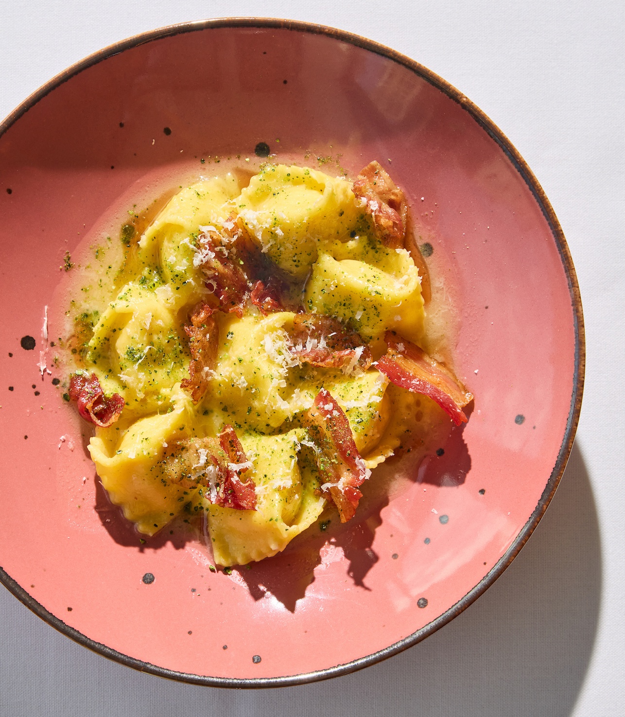 Overhead view of filled pasta topped with bits of pancetta and a green powder.