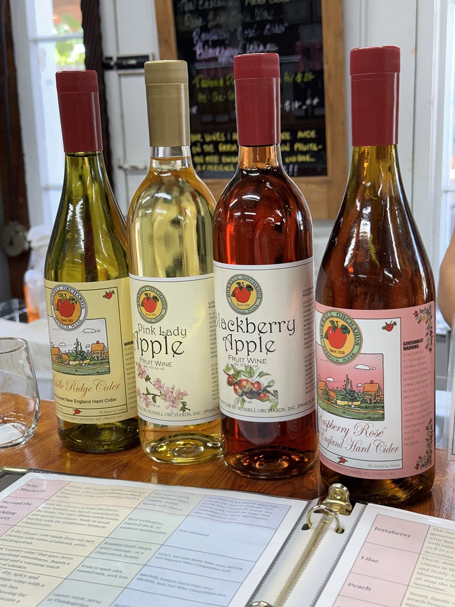 A lineup of wine and cider bottles in a tasting room feature varieties such as blackberry apple and pink lady apple.