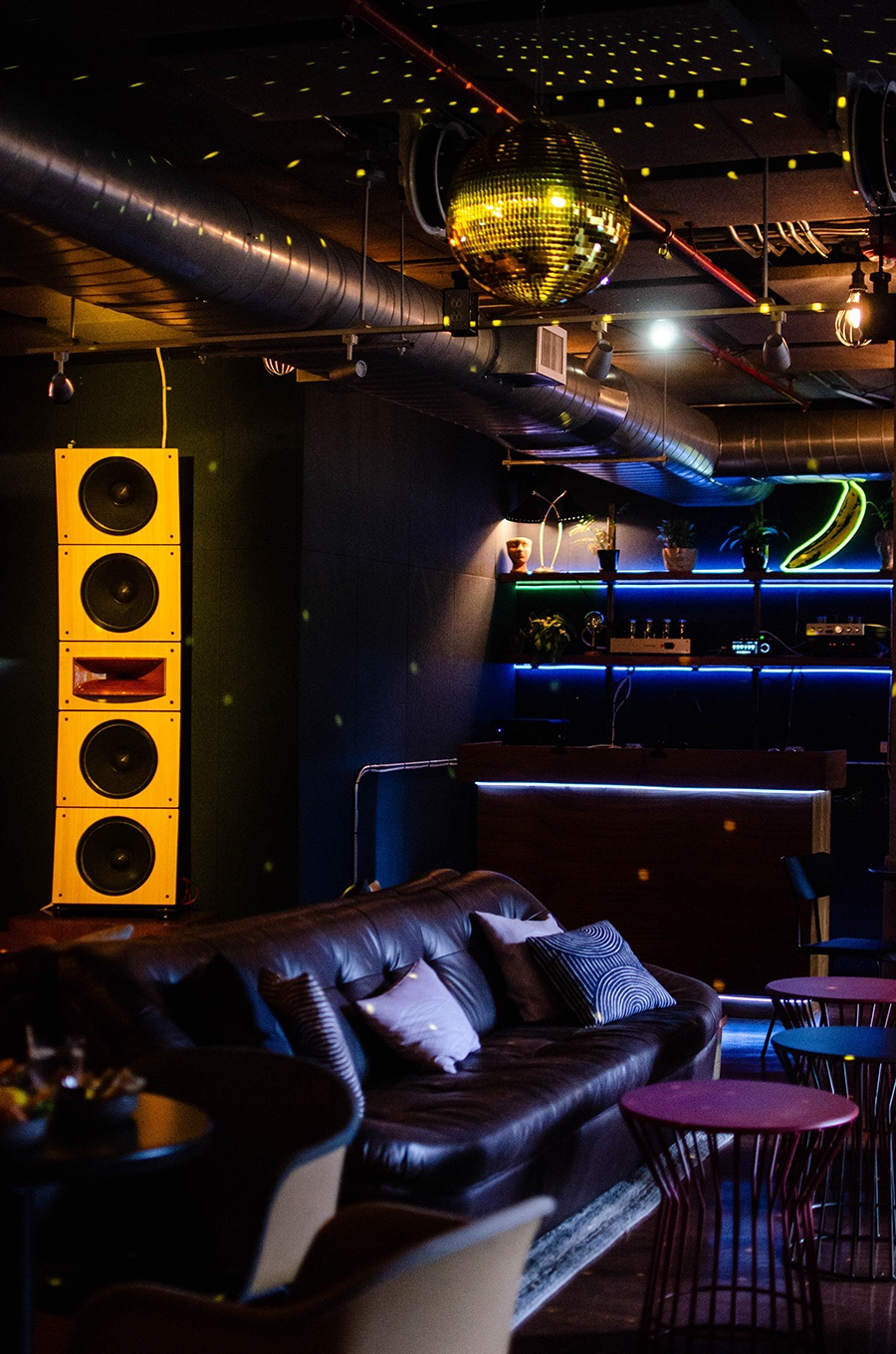 Interior of a dark bar with lounge furniture, a big speaker, and a disco ball.