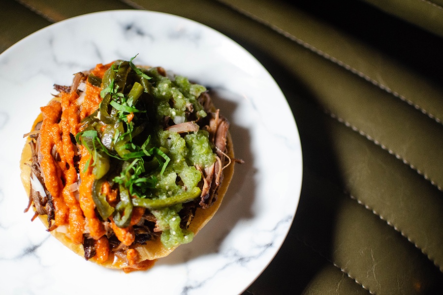 Overhead view of a tortilla topped with shredded brisket, jalapenos, and green and orange sauces.