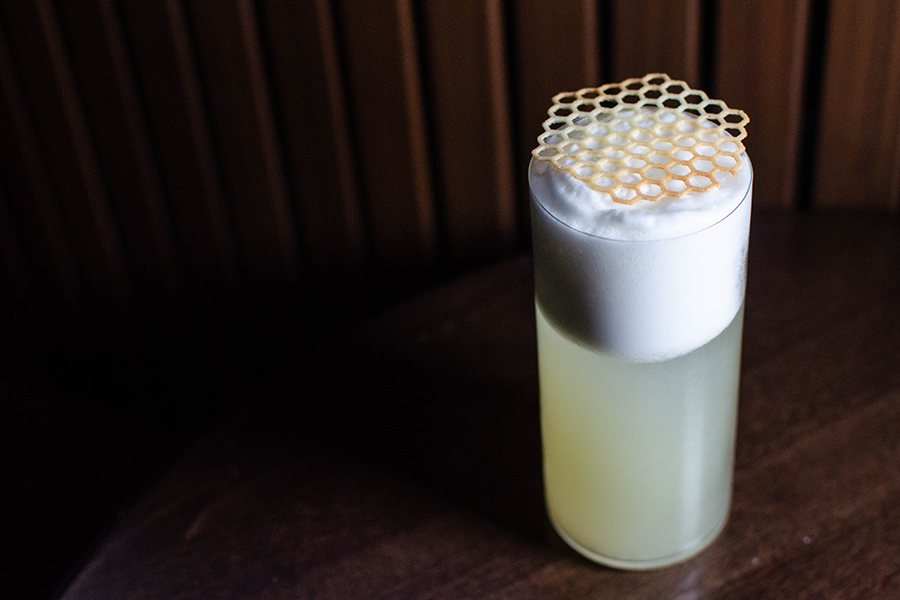 A yellow cocktail with a frothy top is topped by a honeycomb of sugar.