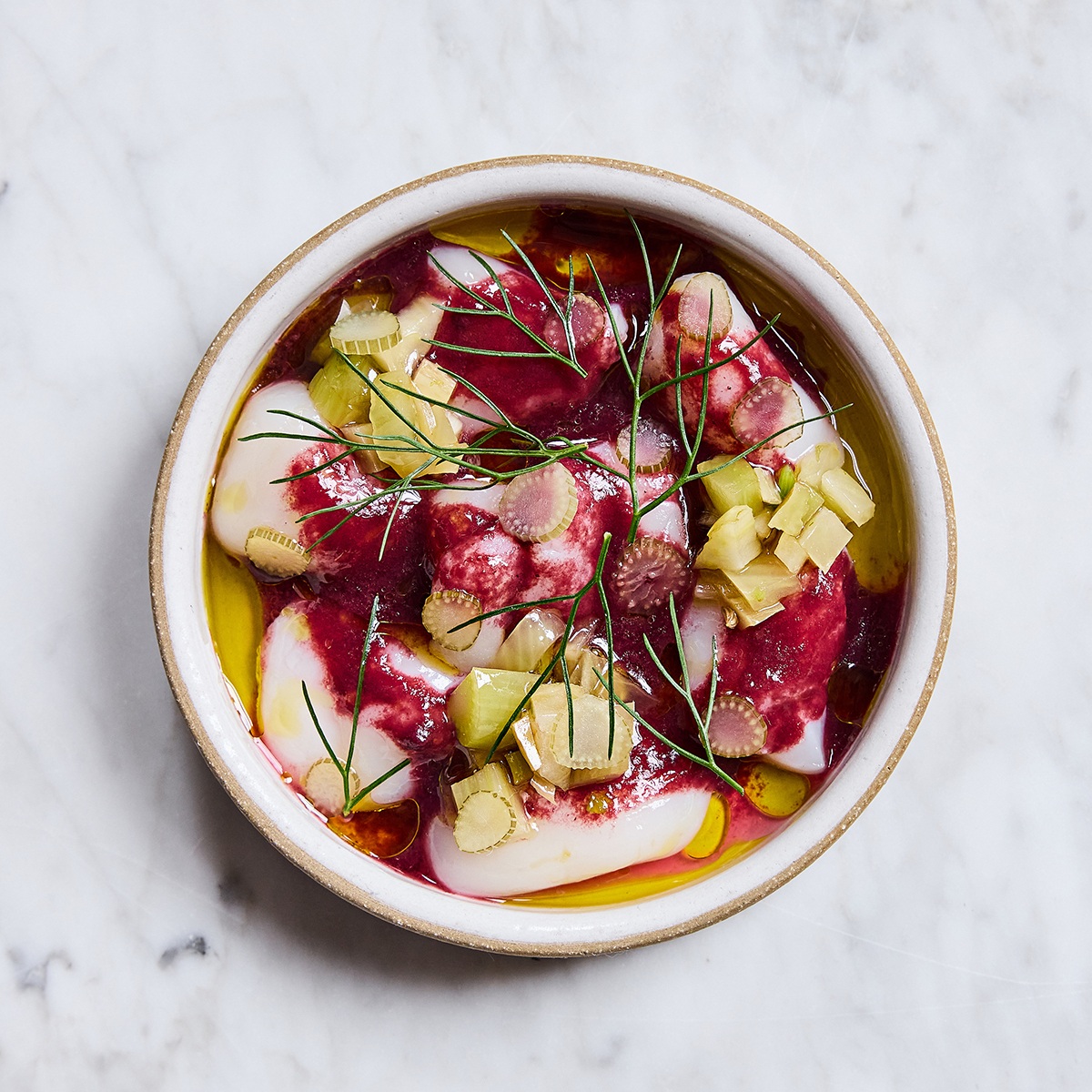 Overhead view of a round dish of scallop crudo with bright purple grape sauce.