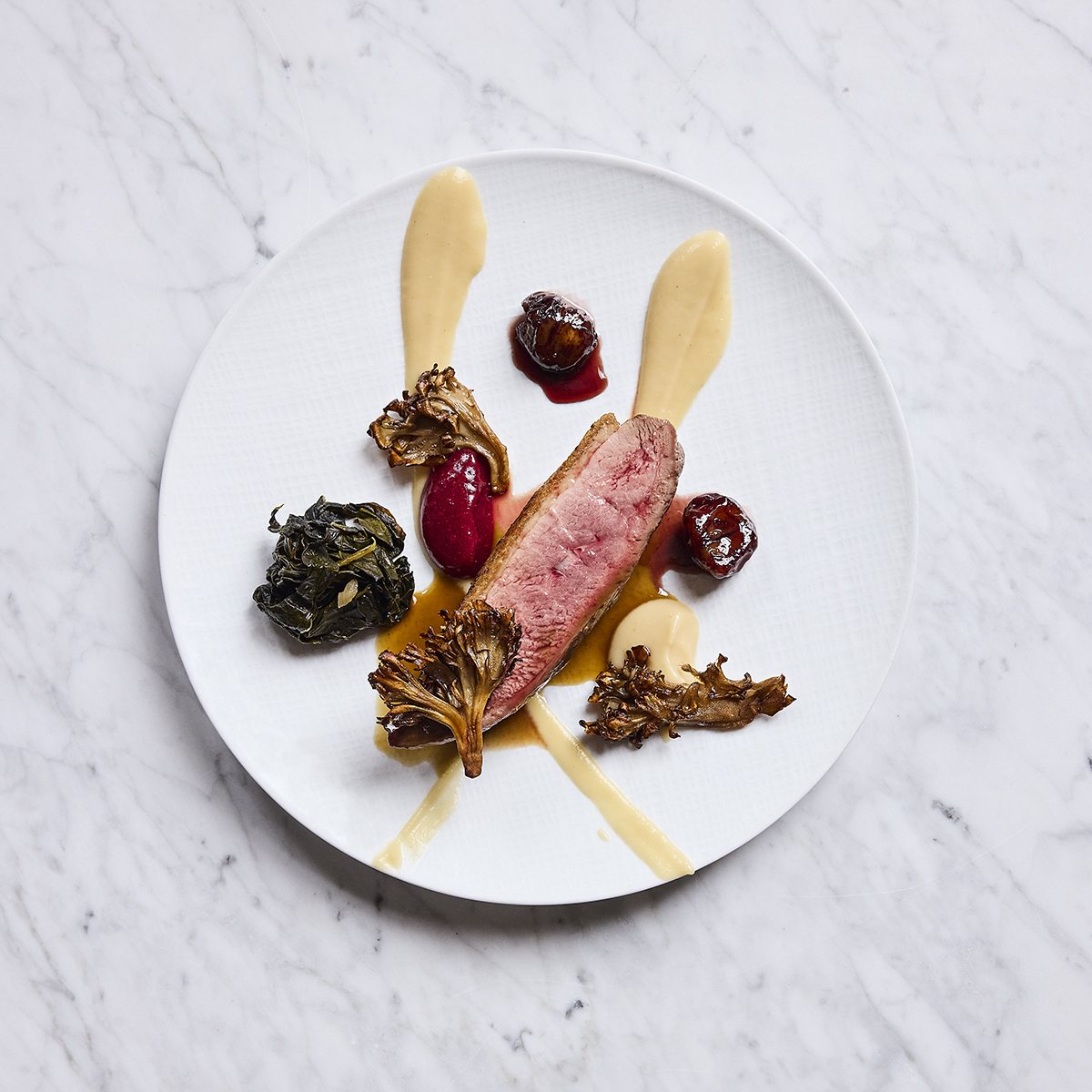 Overhead view of a portion of meat plated elegantly with swooshes of sauce and mushrooms.