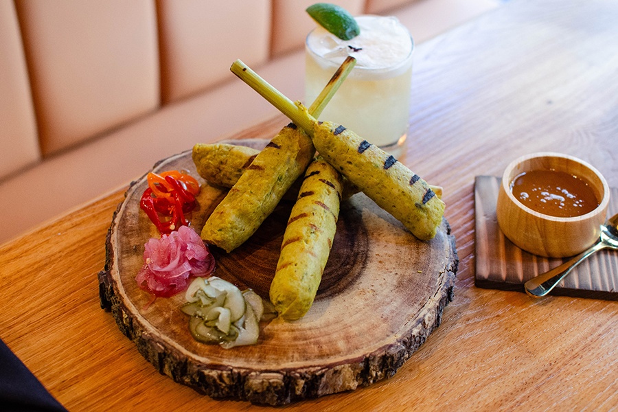 Grilled sticks of minced chicken are served on a tree stump plate with various pickles.