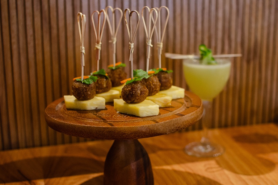 Balls of ground turnip and peanut, garnished with cilantro, sit atop slices of pineapple and are served on a toothpick.