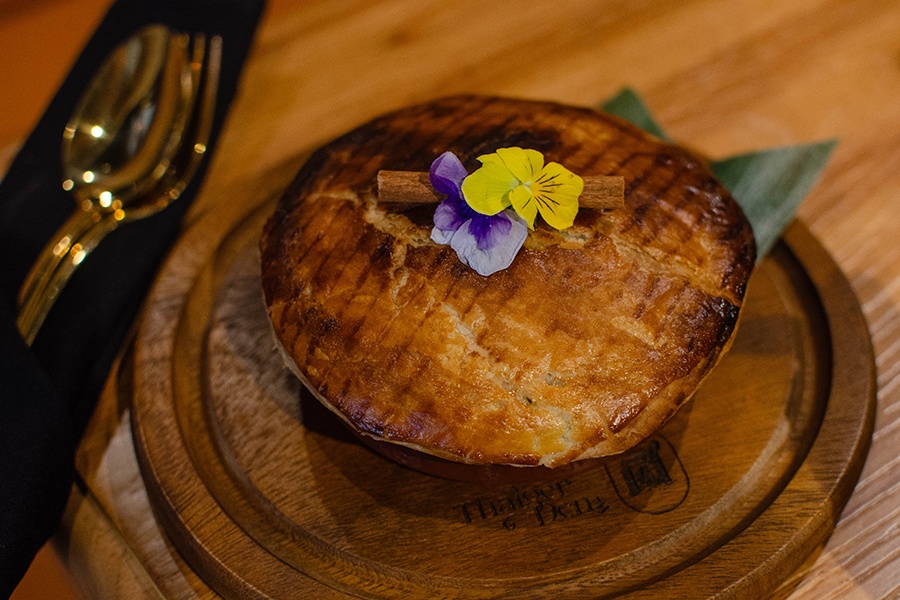 A personal-sized pot pie is garnished with a cinnamon stick and edible flowers.