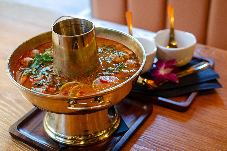 A big gold pot with a hole in the middle for fire is full of a reddish soup with chilis, mushrooms, and lime slices.