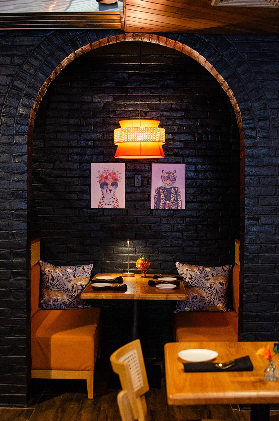 A restaurant interior features black bricks and a dramatic archway over a booth with tiger artwork and pillows.