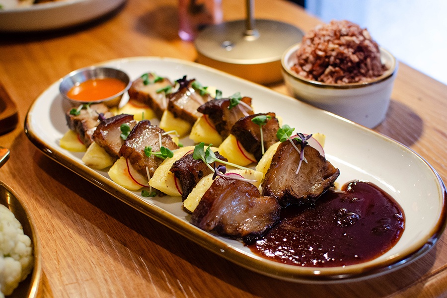 Slices of pork belly alternate with slices of pineapple on a long oval plate.