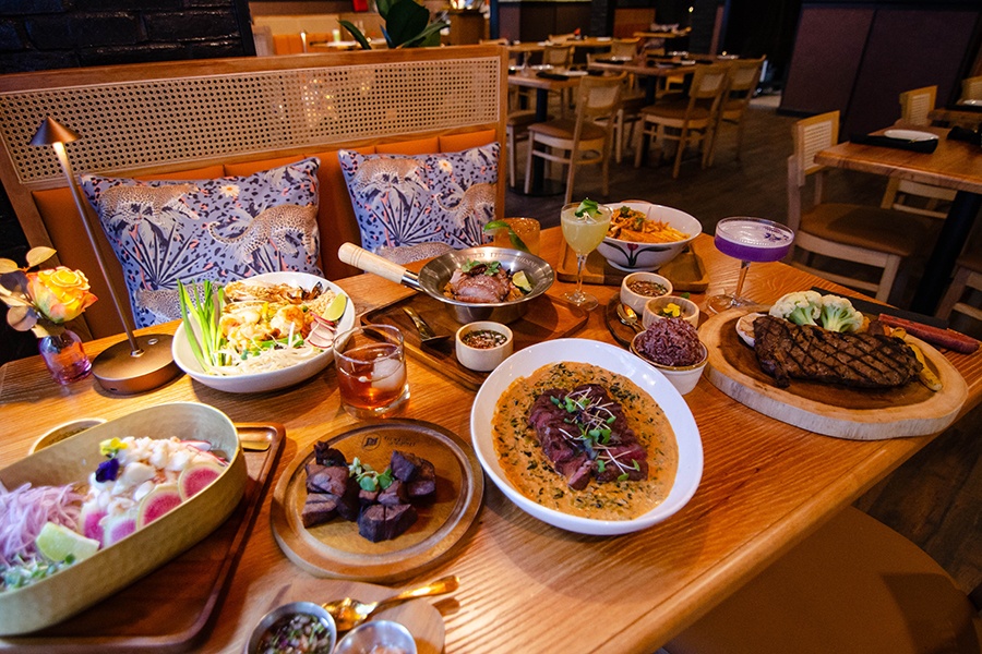 A spread of Thai dishes cover a light wooden table.