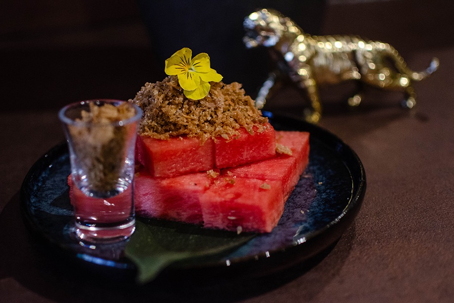 Cubes of watermelon are topped with brown crispy bits and a small edible flower.