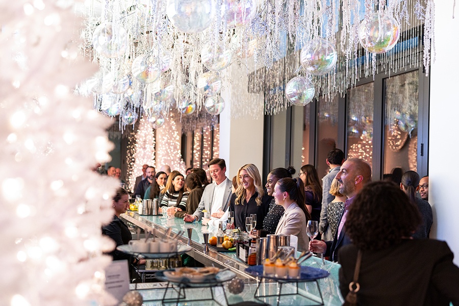 People smile around a bar decorated for the holidays, with white Christmas trees and white and silver baubles.