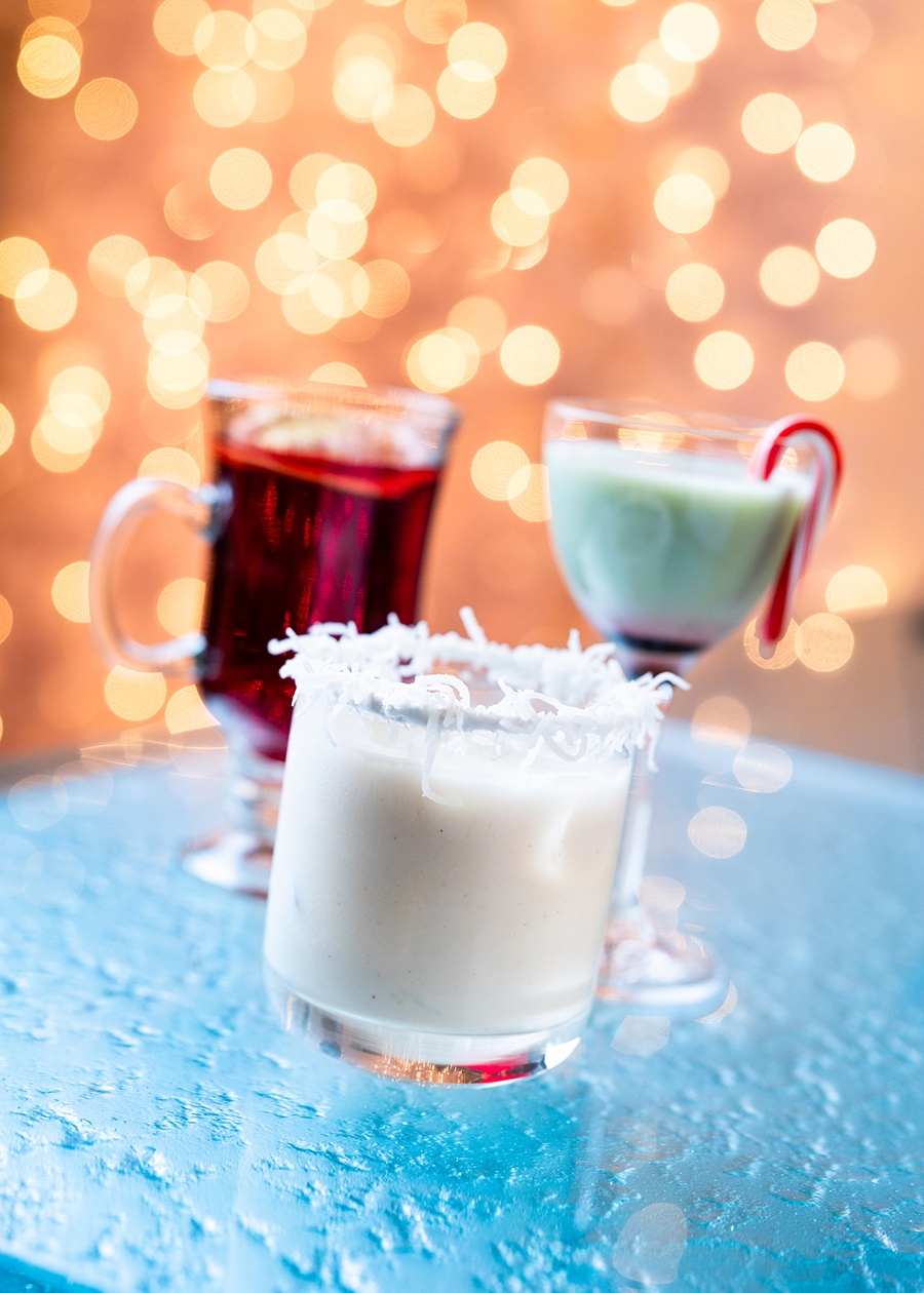 Three colorful cocktails sit on a blue table with glowing lights in the background.